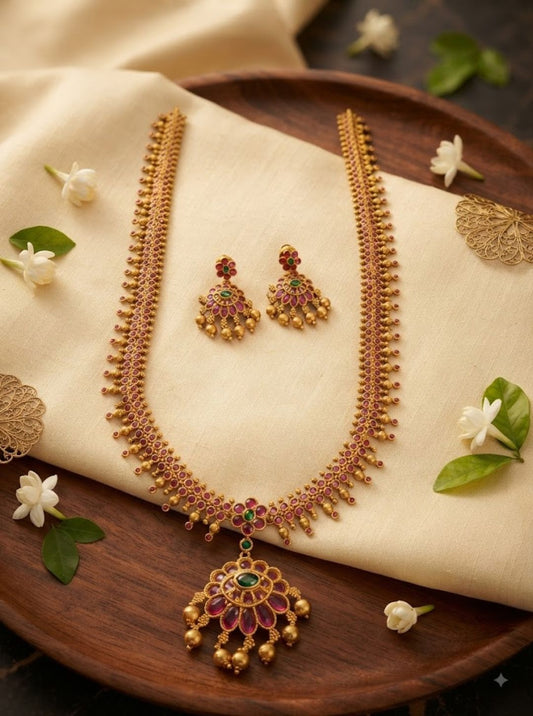 Traditional gold-toned ruby necklace set with green stones and an ornate pendant on black slate.