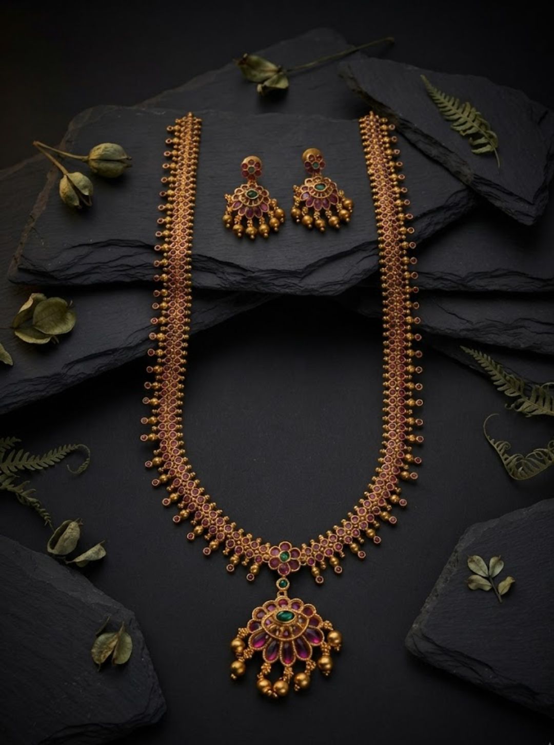 Ornate ruby and emerald-toned necklace with floral pendant and matching gold-toned earrings.