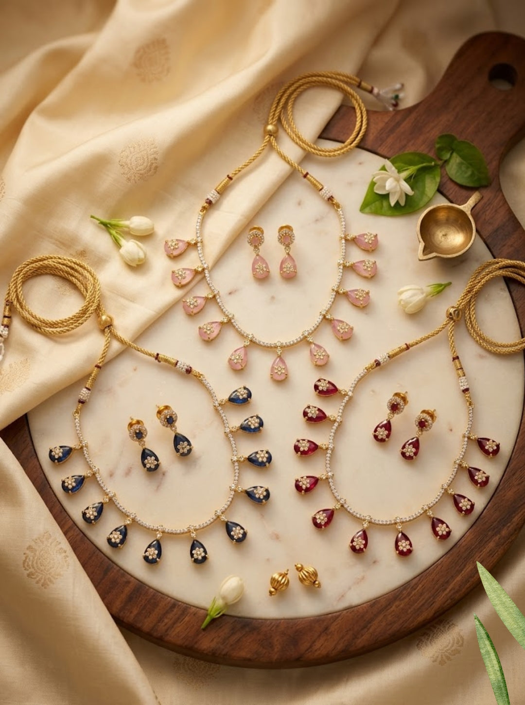 Three colourful teardrop necklace sets in pink, blue and ruby tones with matching earrings.